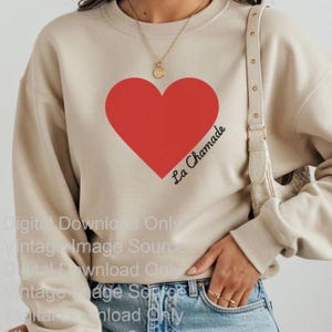 Könnte beinhalten: Beiges Sweatshirt mit großem rotem Herz-Design und dem schwarzen Schriftzug "La Chamade". Das lässige Oberteil ist für den täglichen Gebrauch geeignet.