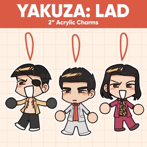 May include: Three 2-inch acrylic charms featuring characters from Yakuza: LAD. Each charm depicts a stylized character with distinct outfits and expressions. The top of the image reads "YAKUZA: LAD" in white text on a red background.