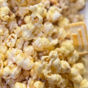 May include: Close-up of caramel popcorn with square-shaped cookies. The popcorn is coated in a glossy caramel glaze, and the cookies have a light brown color with a decorative design. The image is a close-up shot.