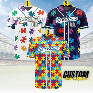 May include: Three baseball jerseys with puzzle piece patterns. One is white with colorful puzzle pieces, another is navy blue with colorful puzzle pieces, and the third is a colorful puzzle piece design. Each jersey has the text "Yourteams" and the number "00".