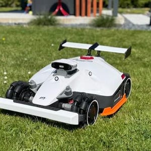 以下が含まれることがあります： 白いとオレンジ色のロボット芝刈り機。スポイラー、黒い車輪、洗練されたデザインが特徴で、緑の芝生の上に置かれています。芝刈り機は未来的な外観で、自動芝刈りを示唆しています。