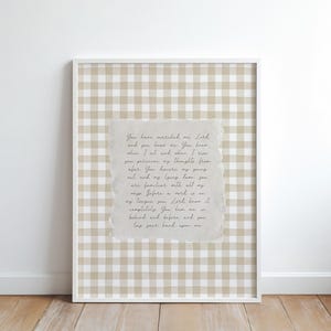 May include: A framed print with a beige and white gingham pattern background. The print features a torn-edged paper with handwritten text in black ink. The frame is white, and the overall aesthetic is rustic.