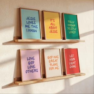 Puede incluir: Seis impresiones artísticas enmarcadas con citas inspiradoras en estantes de madera. Las impresiones presentan fondos coloridos y texto como "Jesus Loves Me This I Know" y "Let Your Light Shine". Los marcos son de color marrón claro.