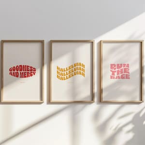 Könnte beinhalten: Drei gerahmte Kunstdrucke mit inspirierenden Texten. Der erste Druck zeigt "GOODNESS AND MERCY" in Rot, der zweite "HALLELUJAH" in Gelb und der dritte "RUN THE RACE" in Rosa. Alle Drucke haben einen Retro-Schriftstil mit Wellen.
