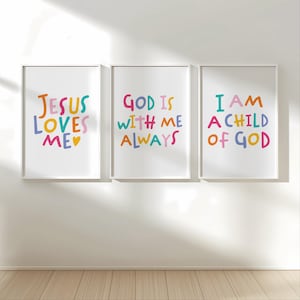 May include: Three framed art prints with white borders and colorful text. The prints read "JESUS LOVES ME", "GOD IS WITH ME ALWAYS", and "I AM A CHILD OF GOD". The text is in various colors, including blue, yellow, pink, and orange, against a white background.