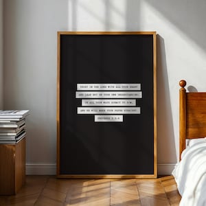 Puede incluir: Un marco negro con un marco de madera. La impresión presenta texto blanco con una cita de Proverbios 3:5-6. La habitación tiene un marco de cama de madera, una mesita de noche con libros y una ventana con luz natural.