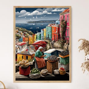 May include: A framed art print depicting a colorful hillside town with buildings in shades of red, yellow, green, and blue. A woman in a green shirt and apron is at a market stall with produce. The background shows a sea with boats and a cloudy sky.