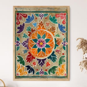 Op de afbeelding: Een ingelijst kunstwerk met een levendig, symmetrisch bloemmotief. Het kunstwerk toont een centrale oranje cirkel met een roze en turquoise bloem, omringd door kleurrijke bladeren en bloemmotieven in rood, paars, groen en blauw. De lijst is licht van kleur.