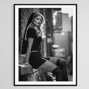 May include: Black and white framed print of a person in a black outfit, sitting on a ledge. The person is wearing a short-sleeved top, a skirt, and thigh-high stockings. A black head covering is draped over the person's shoulder.