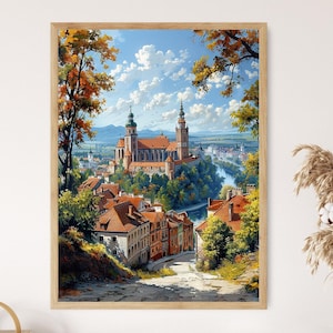 May include: A framed art print of a European townscape. The artwork depicts a cathedral and buildings with red-tiled roofs, surrounded by trees with autumn foliage. A river winds through the town under a blue sky with clouds.