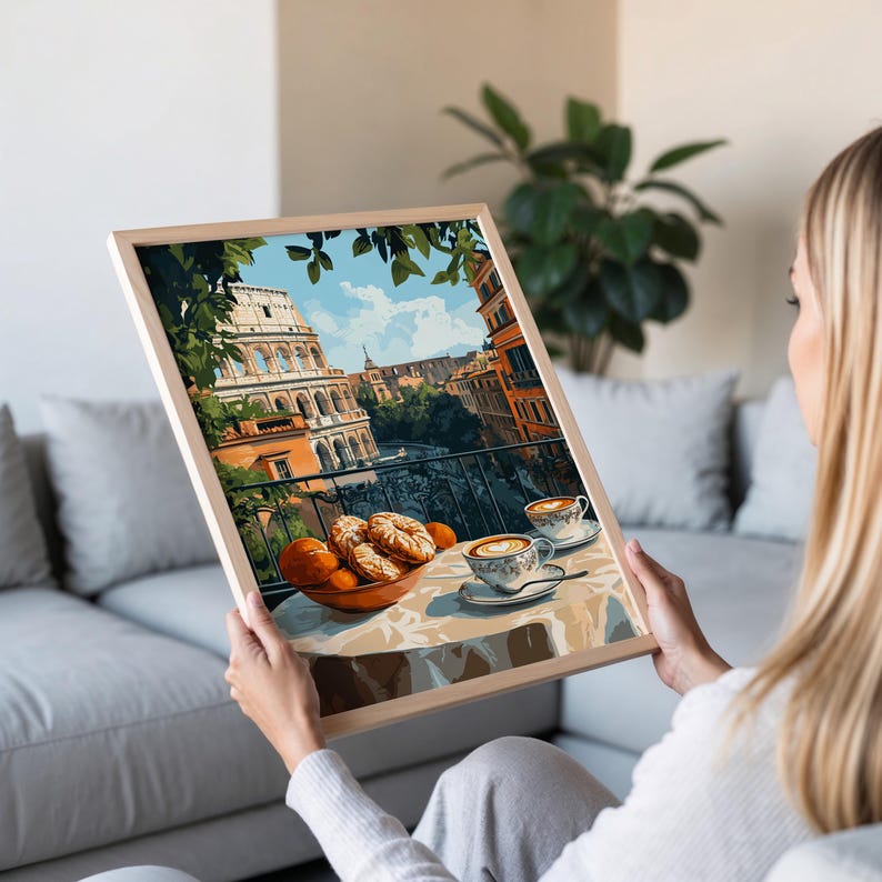May include: A framed print showing an Italian balcony scene with the Colosseum visible. A table is set with pastries, oranges, and two cups of coffee. The print is in a light wooden frame.