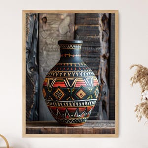 Può includere: Immagine incorniciata di un vaso in ceramica nera con intricati motivi geometrici in rosso, giallo e verde. Il vaso ha un collo stretto e un corpo arrotondato. Lo sfondo è una superficie di legno stagionato.