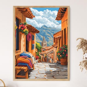 May include: A framed print of a colorful street scene in a mountain town. The artwork depicts buildings with orange walls, red tile roofs, and a cobblestone street. A wooden bench holds folded blankets. Flowers and a church steeple are visible.