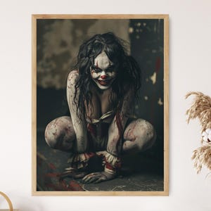 May include: A framed print featuring a scary clown with white face paint, red accents, and dark hair. The clown is crouched down, with blood-like stains on the body and background. The image is set in a dark, ominous environment.