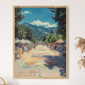 May include: A colorful outdoor art market with a variety of booths selling artwork, crafts, and other goods. The market is set up on a paved street with a mountain range in the background.