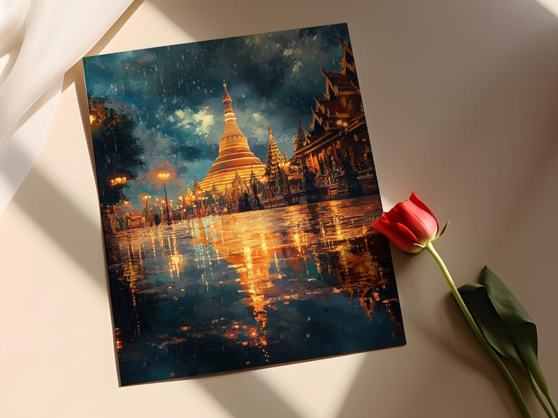 May include: A square art print depicting a golden pagoda and other buildings at night, with reflections in the wet ground. The artwork has a painterly style with dark blues, golds, and oranges. A red rose lies nearby.