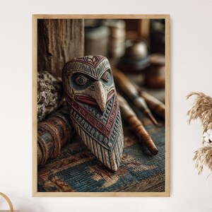 May include: A framed wooden carving of a bird-like face with intricate details. The mask features a beak, eyes, and geometric patterns in shades of brown, red, and blue. The artwork is displayed on a textured surface with wooden elements in the background.