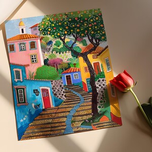 May include: Colorful painting of a European village scene. Buildings in shades of pink, blue, and yellow line a cobblestone street. A large tree with orange-colored fruit is in the center. A red rose is in the foreground.