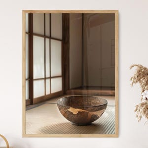 May include: A framed photograph of a decorative wooden bowl with gold accents. The bowl sits on a tatami mat in front of a traditional Japanese window. The frame is made of light-colored wood.