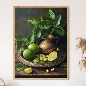 Puede incluir: Pintura enmarcada de naturaleza muerta con una jarra de latón y una bandeja decorativa con limas y rodajas de lima. Hojas verdes exuberantes y un fondo oscuro crean un contraste llamativo. La obra de arte está sobre una superficie de madera.