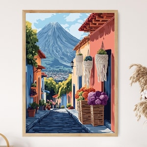 May include: A framed art print showing a vibrant street scene with a mountain in the background. The artwork features buildings in shades of orange, blue, and yellow, with a cobbled street leading towards the mountain. Wicker baskets filled with flowers hang on the walls.
