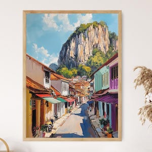 May include: A colourful painting depicting a street lined with buildings in a tropical setting. The buildings are painted in bright colours, including yellow, green, blue, and red. The street is narrow and winding, with trees and plants growing on either side. In the background, a large, rocky mountain rises up in the distance.