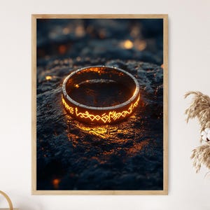 Peut inclure: Impression encadrée d'une bague dorée brillante avec des motifs gravés complexes. La bague est posée sur un fond sombre et texturé, créant un contraste saisissant. Le design suggère un thème fantastique ou magique.