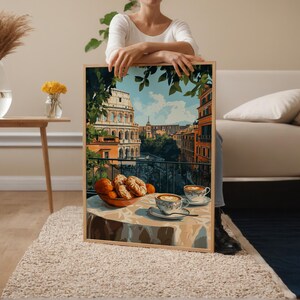 May include: A framed print showing an Italian balcony scene with the Colosseum in the background. The artwork features a table set with pastries, oranges, and two cups of coffee. The colour palette includes warm tones of orange, brown, and blue.