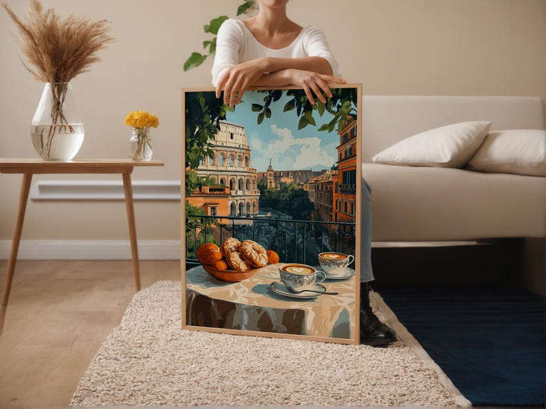 May include: A framed print showing an Italian balcony scene with the Colosseum in the background. The artwork features a table set with pastries, oranges, and two cups of coffee. The colour palette includes warm tones of orange, brown, and blue.