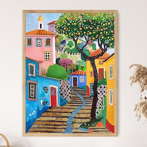 May include: A framed painting depicts a colorful European village scene. Buildings in shades of pink, blue, and yellow line a cobblestone street. A large tree with orange fruit and a winding blue stream add to the vibrant landscape.