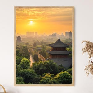 May include: Framed print of a Chinese pagoda at sunrise. The image features a traditional multi-tiered structure with a dark roof, surrounded by lush green trees. The sky is a gradient of yellow and orange, with a bright sun and a distant cityscape.