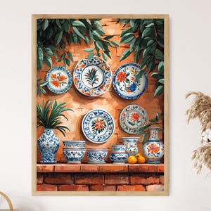 May include: A framed print featuring a collection of decorative plates, vases, and bowls with blue and orange floral designs. The artwork includes a brick wall background, greenery, and a wooden frame, creating a vintage aesthetic.