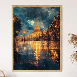May include: A framed art print depicts a golden pagoda and buildings reflecting in a wet street. The artwork has a painterly style with a dark blue sky and warm golden light illuminating the scene. The print is in a light wood frame.