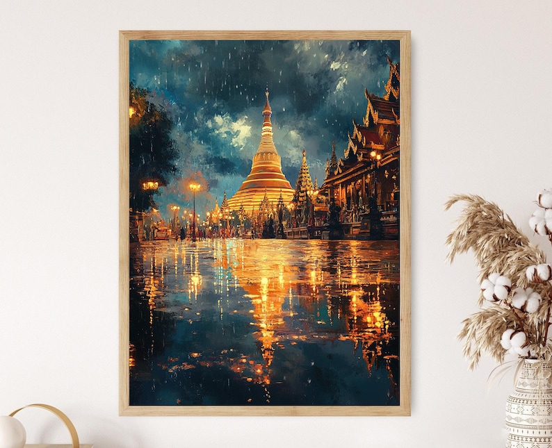 May include: A framed art print depicts a golden pagoda and buildings reflecting in a wet street. The artwork has a painterly style with a dark blue sky and warm golden light illuminating the scene. The print is in a light wood frame.
