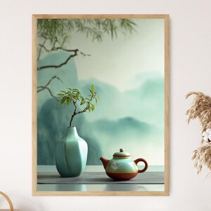 Pode incluir: Uma impressão emoldurada com uma natureza morta serena. Um vaso verde-água claro contém um pequeno galho com folhas, ao lado de uma chaleira turquesa e vermelha com detalhes florais. O fundo retrata uma paisagem montanhosa nebulosa.