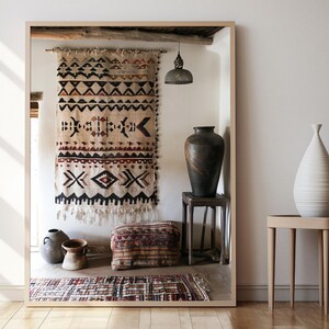 May include: A large mirror frames a rustic interior scene. A patterned textile hangs on the wall, complemented by a dark vase on a small stool and a white vase on a side table. A patterned rug and a decorative pillow are on the floor.