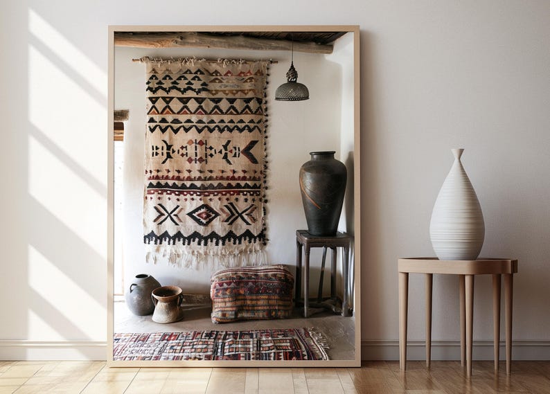 May include: A large mirror frames a rustic interior scene. A patterned textile hangs on the wall, complemented by a dark vase on a small stool and a white vase on a side table. A patterned rug and a decorative pillow are on the floor.