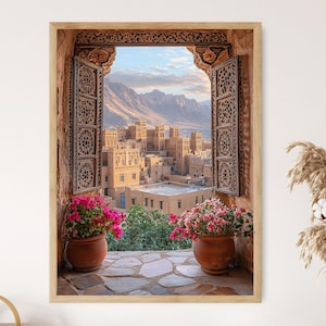 May include: A view of a Middle Eastern city through an intricately carved wooden doorway. The doorway is open, revealing a cityscape with buildings and a mountain range in the distance. Pink flowers are in pots on either side of the doorway.