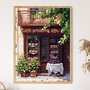 May include: A framed print of a bakery storefront. The dark brown wooden facade features glass display cases filled with pastries. A small table with a white lace tablecloth holds a display of purple fruit. Green plants and foliage add color.