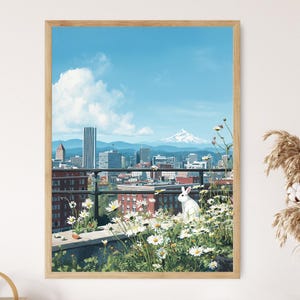 Könnte beinhalten: Ein weißes Kaninchen sitzt auf einem Dachgarten mit Blick auf eine Skyline. Die Stadt ist voller Gebäude und einem Berg in der Ferne. Der Himmel ist blau mit weißen Wolken. Das Kaninchen ist von weißen Gänseblümchen umgeben.