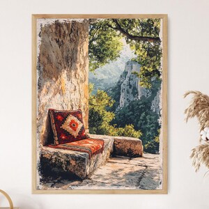 May include: Framed print depicting an outdoor scene. A stone bench with a patterned red and orange cushion and pillow is in a stone alcove. The background shows a mountain range and green trees.