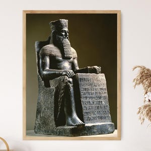 Puede incluir: Una estatua de piedra oscura de una figura sentada con un tocado cilíndrico alto y una barba larga y texturizada. La figura está sentada en un trono, con una mano apoyada en una gran losa de piedra rectangular con inscripciones cuneiformes.
