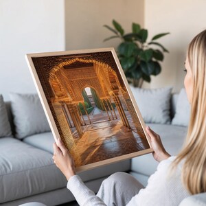 May include: A framed photograph of a grand, ornate archway with intricate details in a golden hue. The archway leads to a courtyard with lush greenery and a pathway.