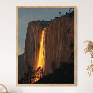 May include: A framed print of a natural landscape featuring a waterfall illuminated by sunlight. The waterfall cascades down a large rock formation, with trees at the base and top. The light creates a golden glow.
