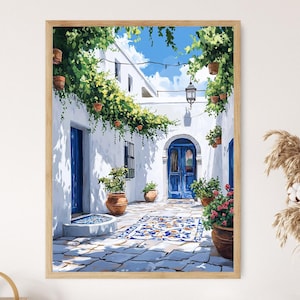 Könnte beinhalten: Ein gerahmter Druck einer mediterranen Hofszene. Das Kunstwerk zeigt weiße Gebäude mit blauen Türen und Fenstern, geschmückt mit grünen Weinreben und Topfpflanzen. Ein blauer Himmel ist oben zu sehen, und ein gemusterter Teppich schmückt den Steinboden.