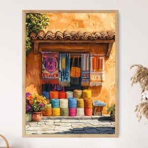 May include: A framed watercolor painting depicts a vibrant outdoor market scene. Colorful textiles hang under a wooden awning, with spools of yarn in various hues stacked in the foreground. A pot of flowers and a small wooden stool add to the scene's charm.