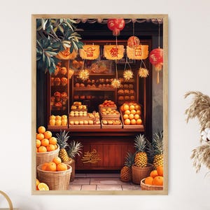 Op de afbeelding: Een ingelijste print van een winkel met een verscheidenheid aan fruit en gebak. Manden met sinaasappels en ananas staan op de voorgrond. De winkel is versierd met rode lantaarns en gouden accenten.