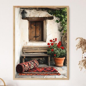 May include: A framed print showing a rustic outdoor scene. A wooden bench is beneath a window with a closed wooden door. A rolled rug and a flat rug with a geometric pattern are on the stone floor. A terracotta pot holds red flowers.