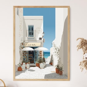 Pode incluir: Uma impressão de arte emoldurada retrata um beco ensolarado com edifícios brancos, uma loja com um toldo listrado e uma vista para o mar. A obra de arte apresenta plantas em vasos, guarda-sóis decorativos e o texto "Lido Wolen". A paleta de cores inclui branco, azul e bege.