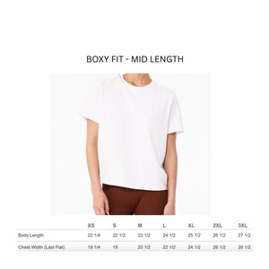 May include: A plain white short-sleeve t-shirt with a boxy fit and mid-length cut. The image includes a sizing chart with body length and chest width measurements in inches for sizes XS through 3XL, labeled as BOXY FIT - MID LENGTH.
